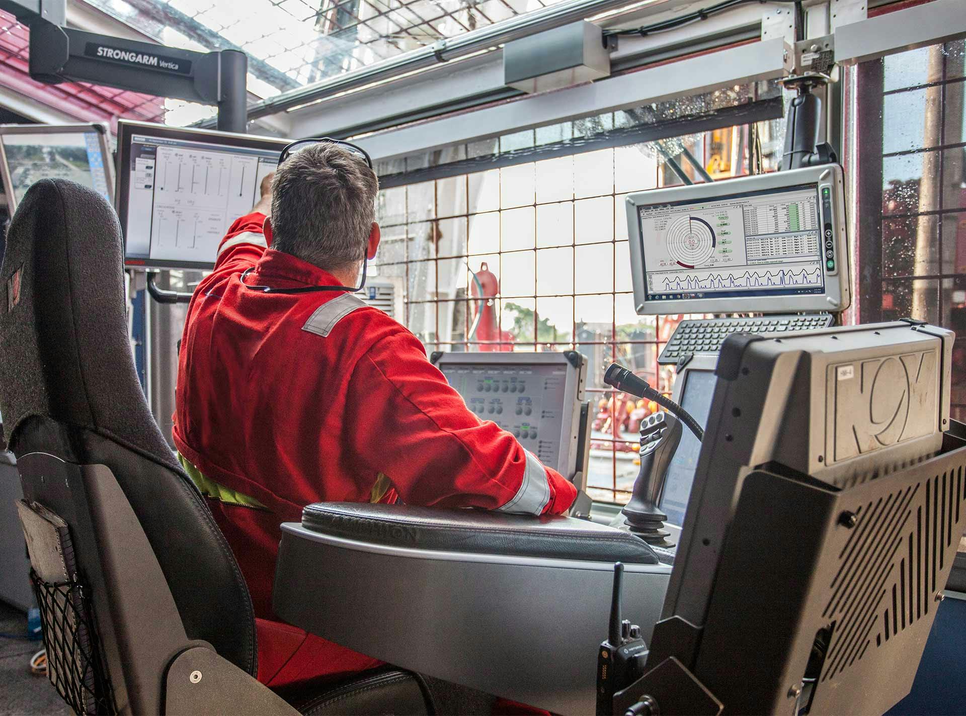 Photo of a man in coveralls in the drillers cabin interacting with a touch screen.